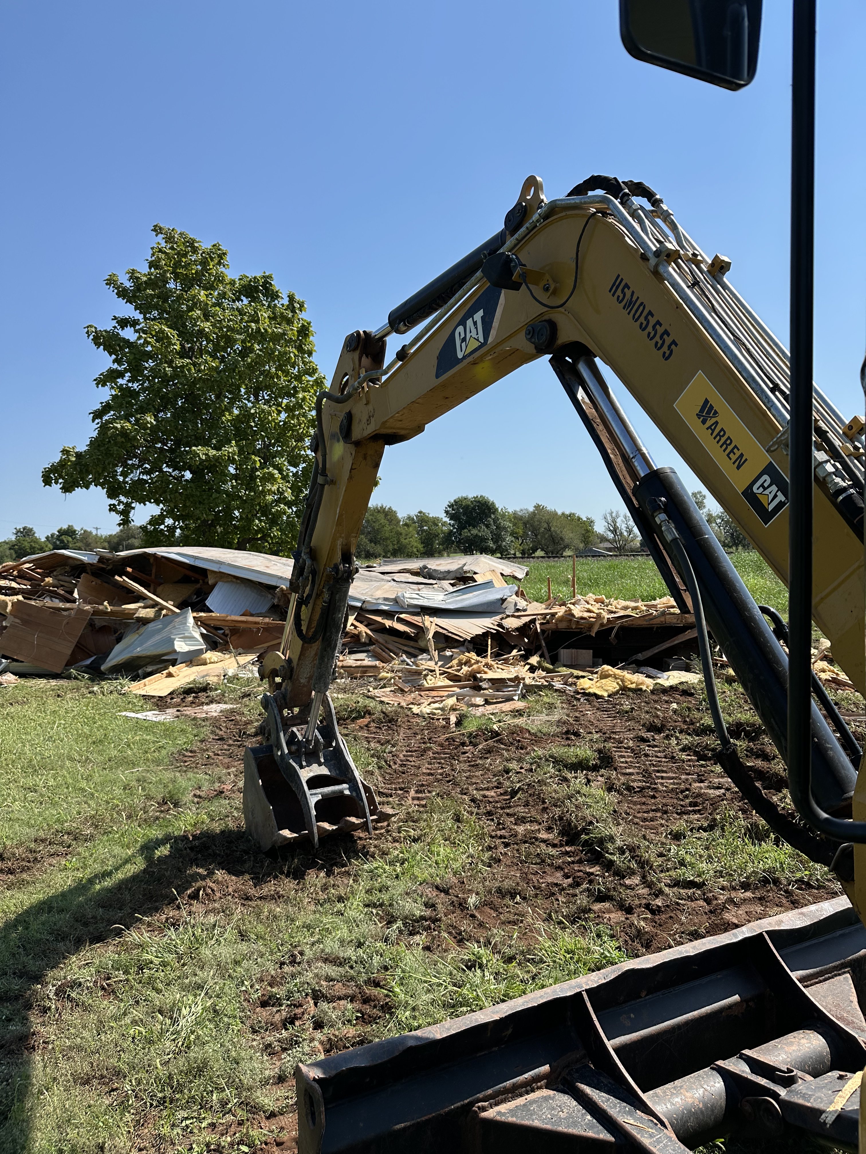 CAT excavator demolishing debris pile during Big Project Solutions demolition services in OKC grassy field